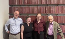 four people standing in front of a wall of books