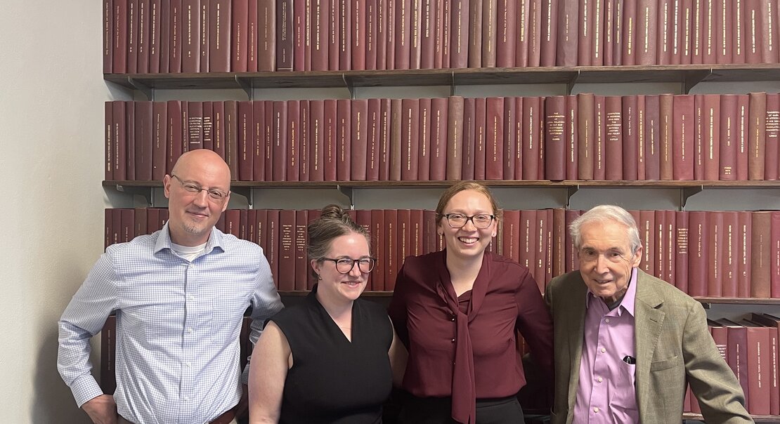 four people standing in front of a wall of books