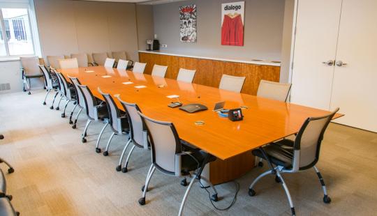 An empty conference room with a large table and chairs in the center.